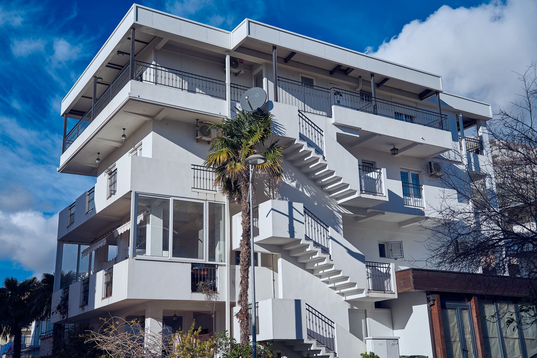 Contemporary white apartment building with unique exterior staircase design, under clear blue sky.